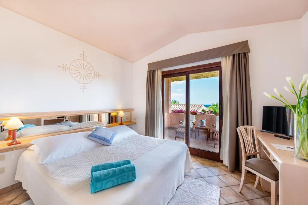 Camera matrimoniale con letto bianco, scrivania e balcone con vista mare