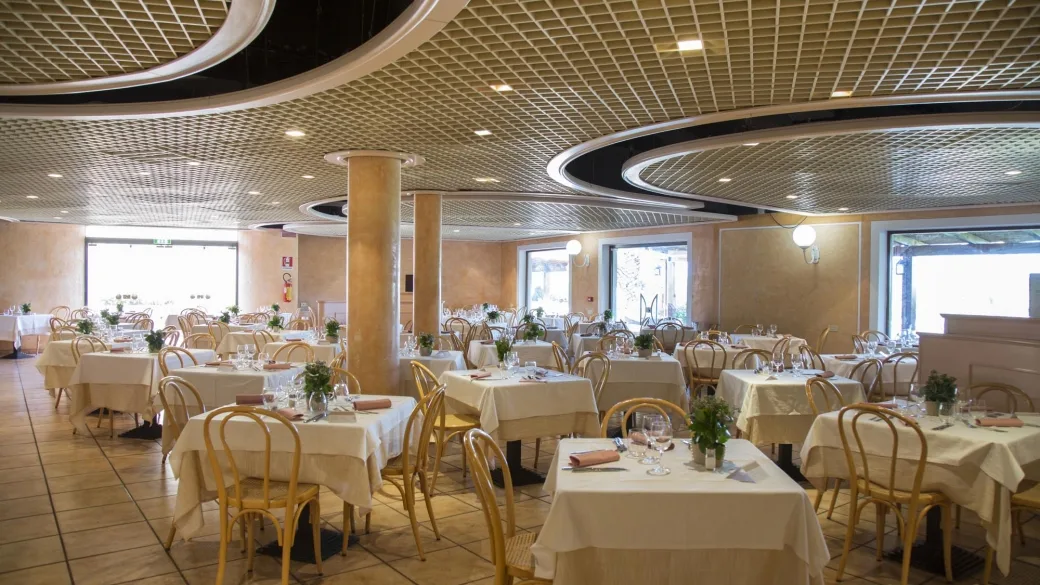 Sala ristorante con tavoli apparecchiati, tovaglie bianche e sedie in legno