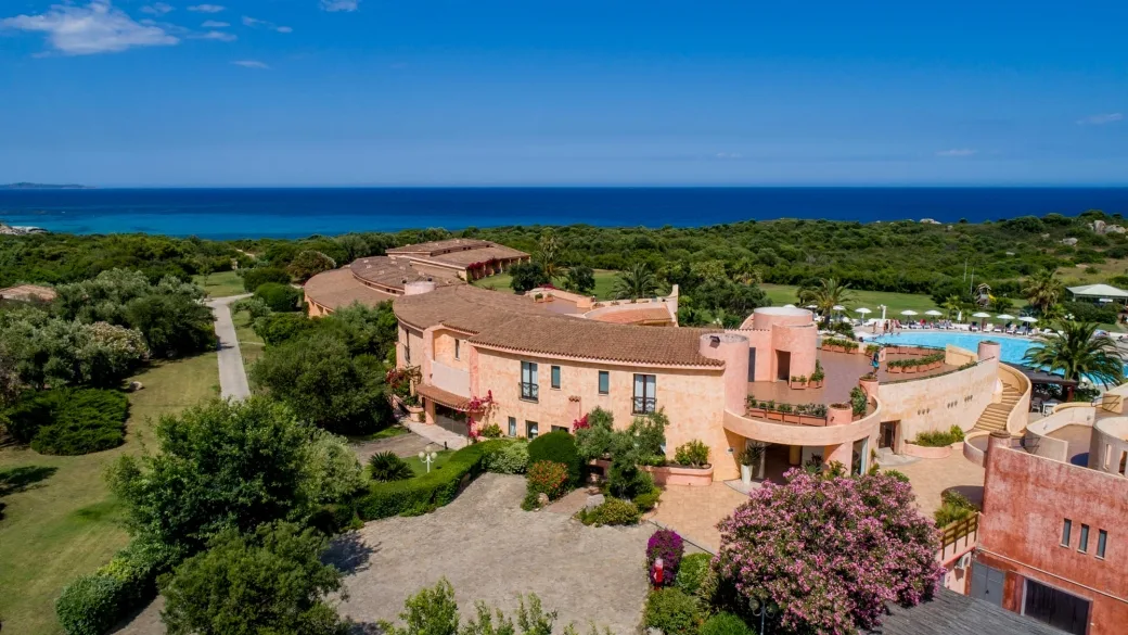 Edificio color rosa del resort con giardini fioriti e mare all'orizzonte