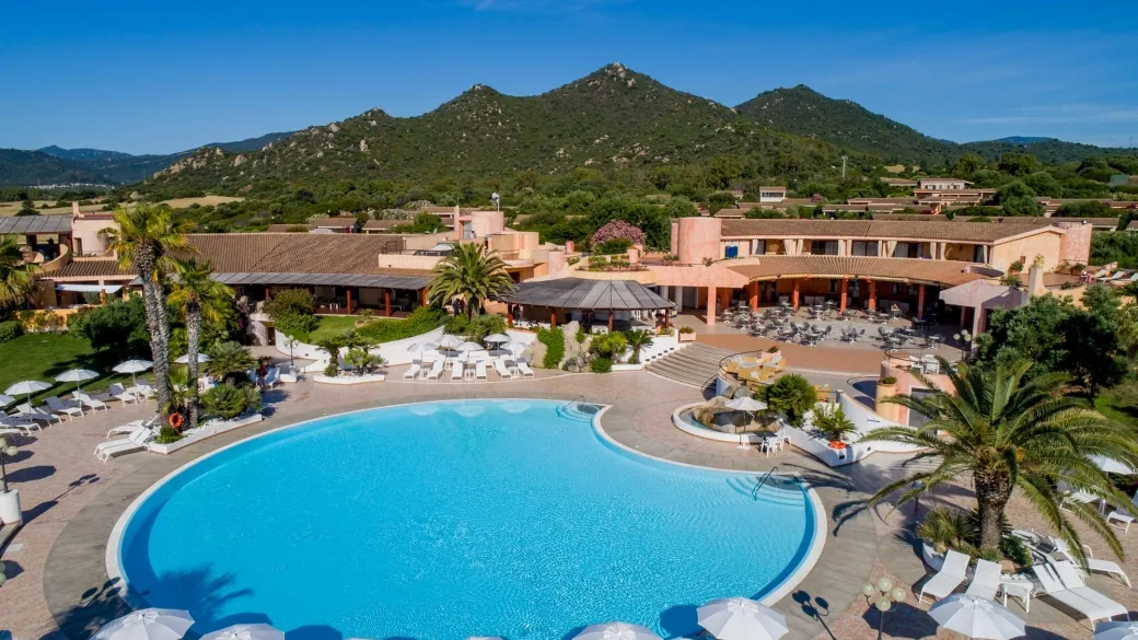 Piscina del resort con lettini bianchi, palme e colline verdi sullo sfondo