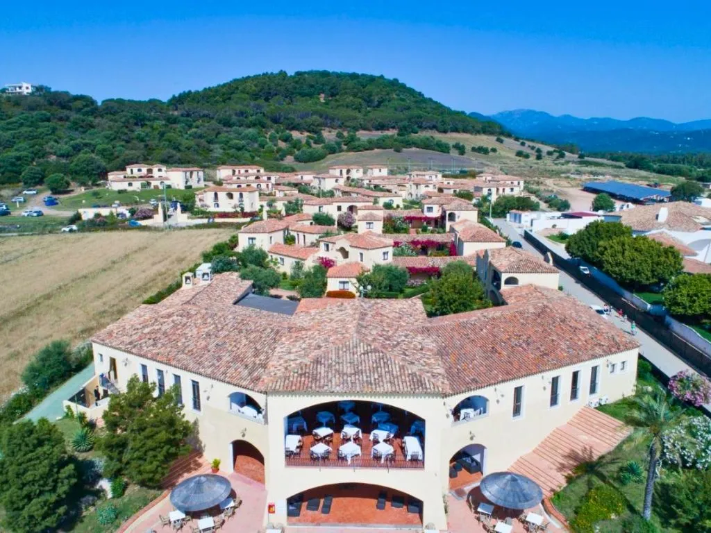 Veduta aerea del resort con tetti in coccio, ville mediterranee e collina verde alle spalle