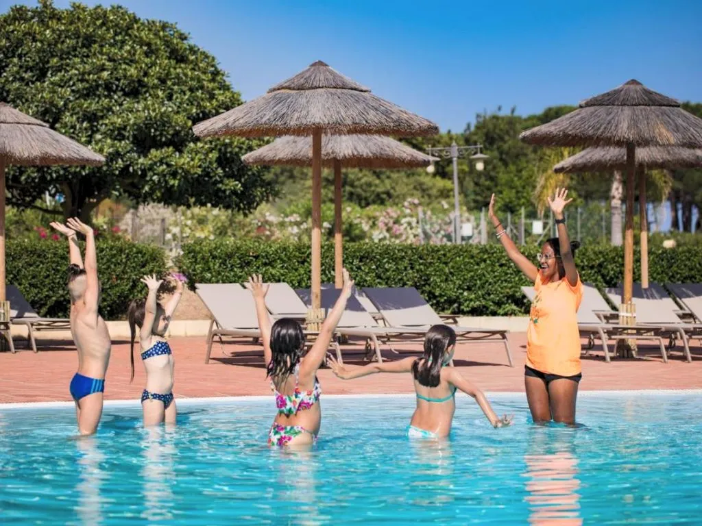 Bambini e animatrice durante attività ludica in piscina con ombrelloni in paglia