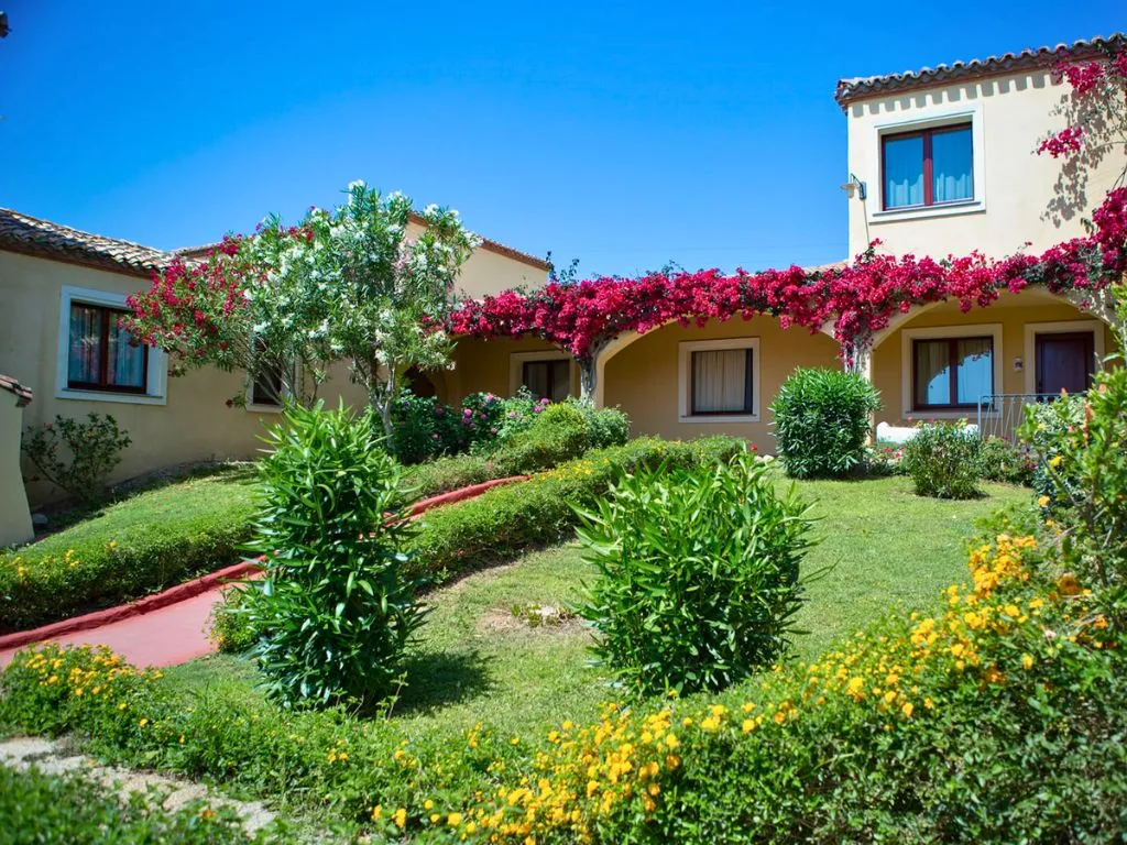 Giardino fiorito con bouganville rosse, prato verde e edifici del resort in stile mediterraneo