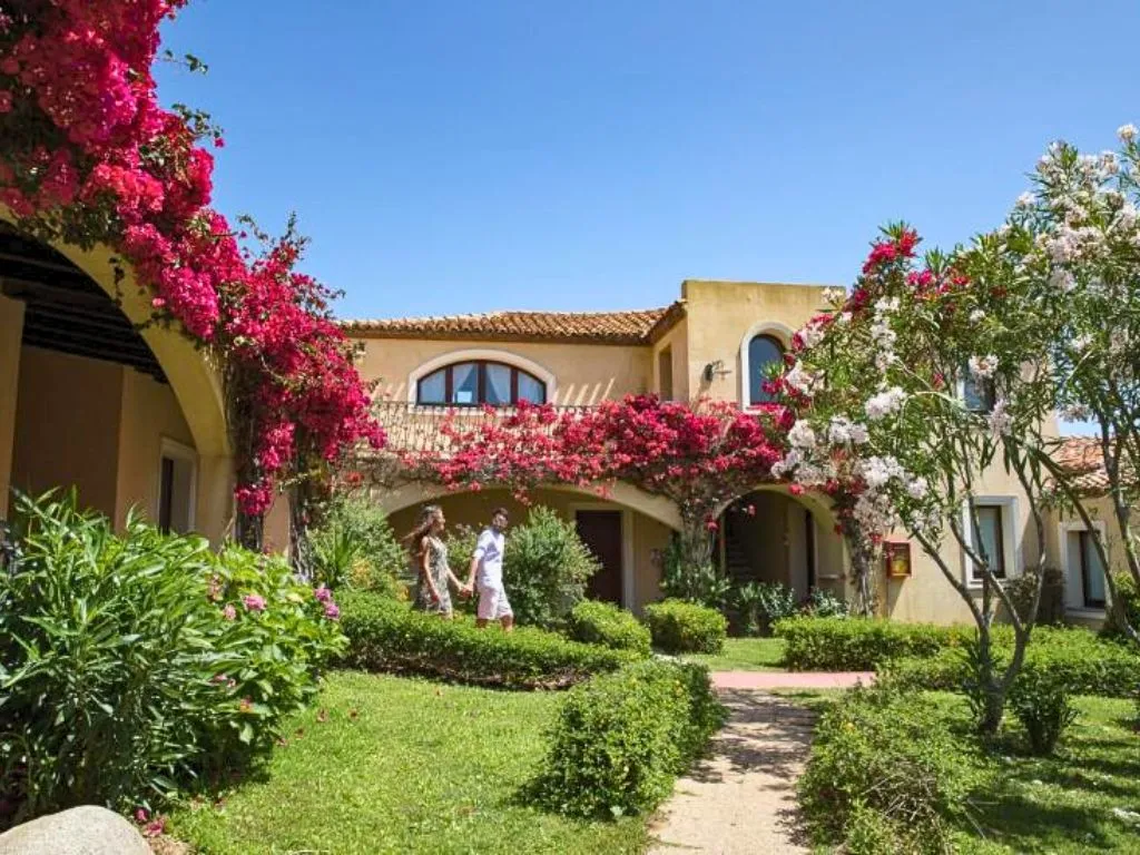 Coppia che passeggia in un giardino curato con archi fioriti di bouganville e edifici color ocra