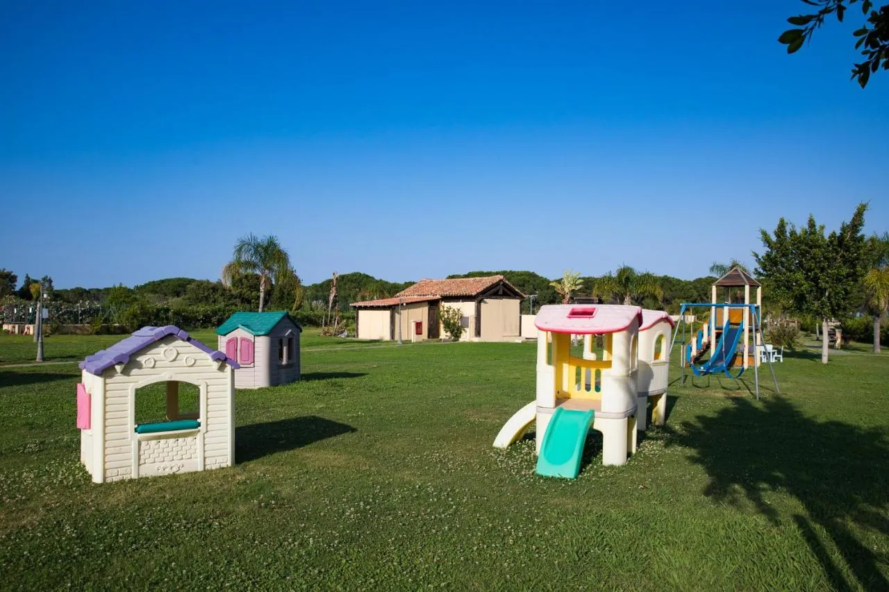 Area giochi per bambini su prato verde con casette colorate, scivoli e altalene
