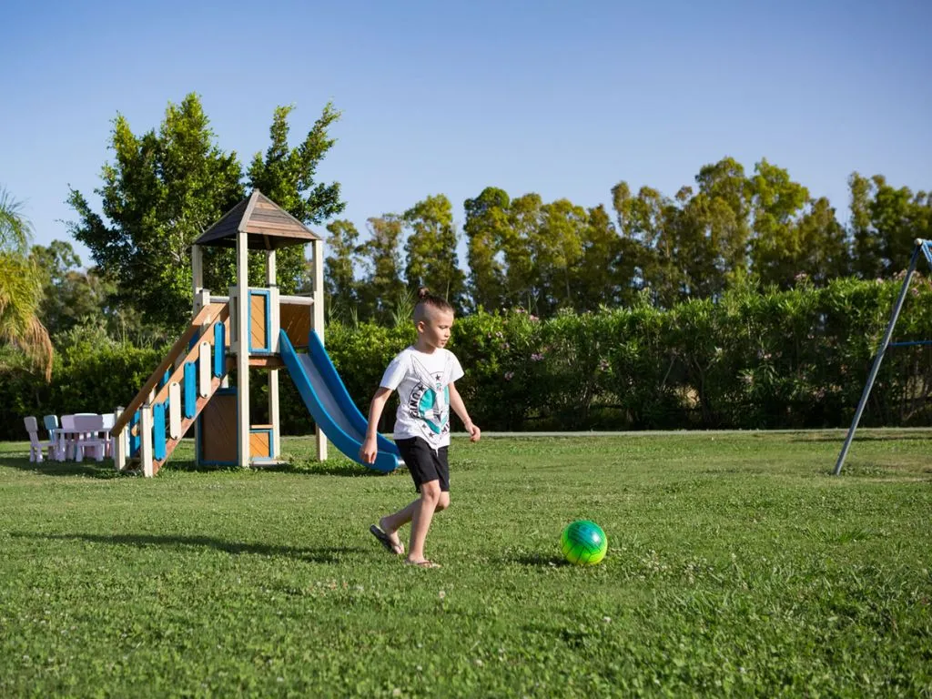 Bambino che gioca a calcio sul prato vicino all'area giochi con scivolo