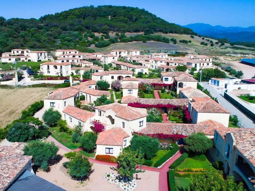 Veduta aerea delle ville del resort con tetti in coccio, giardini fioriti e collina verde