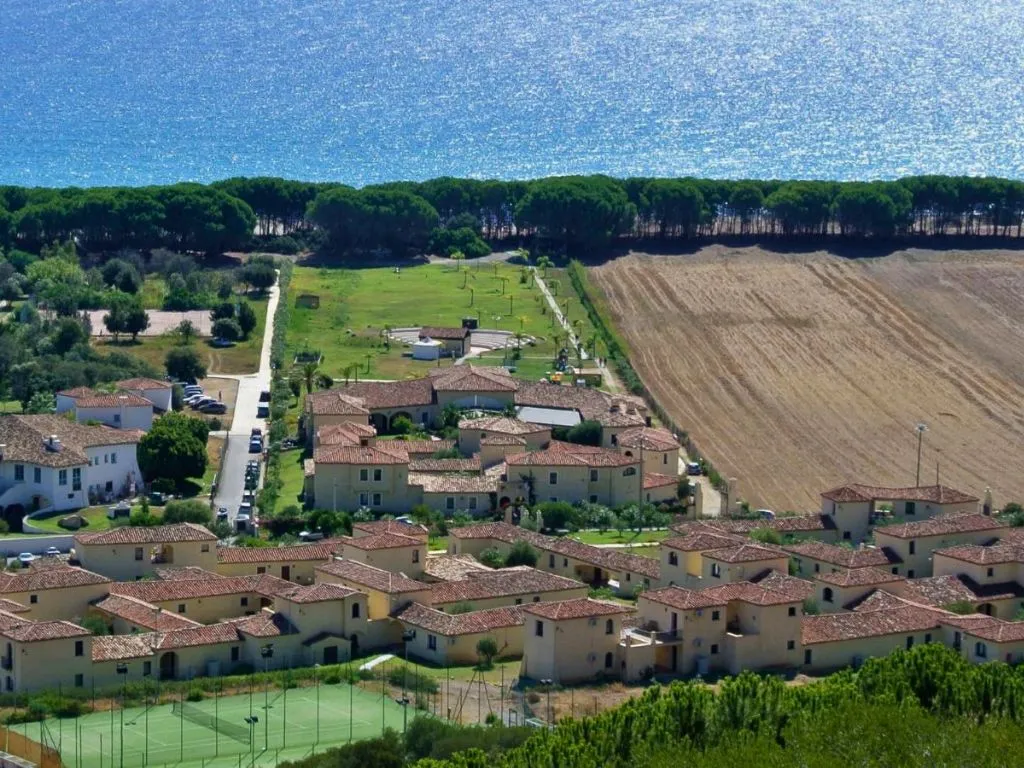 Panoramica dall'alto del resort con ville, campo da tennis, pineta e mare scintillante
