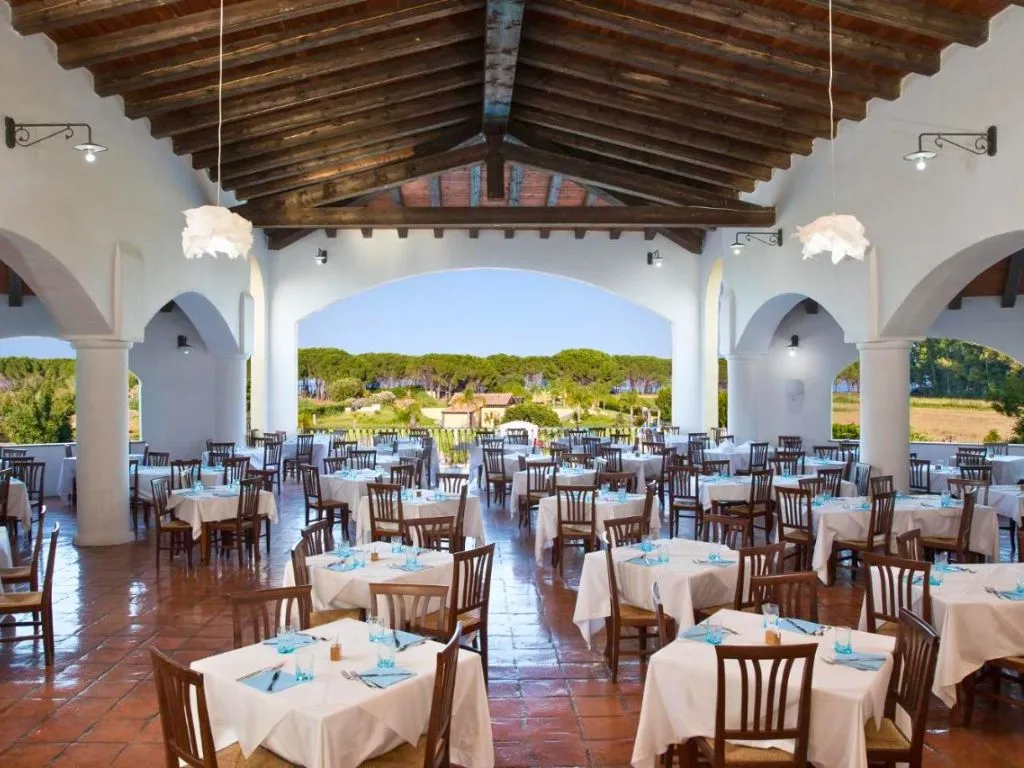 Sala ristorante con soffitto in travi di legno, tavoli bianchi e archi aperti sul verde