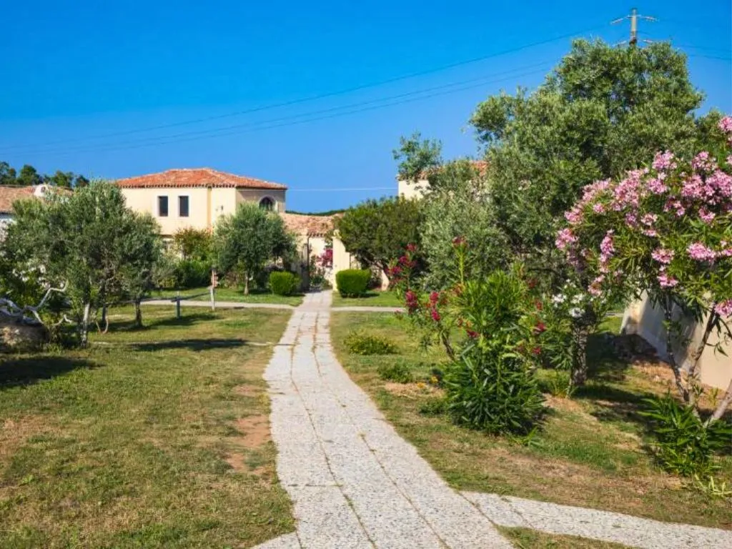 Vialetto in pietra tra prato e ulivi con oleandri fioriti e ville del resort sullo sfondo