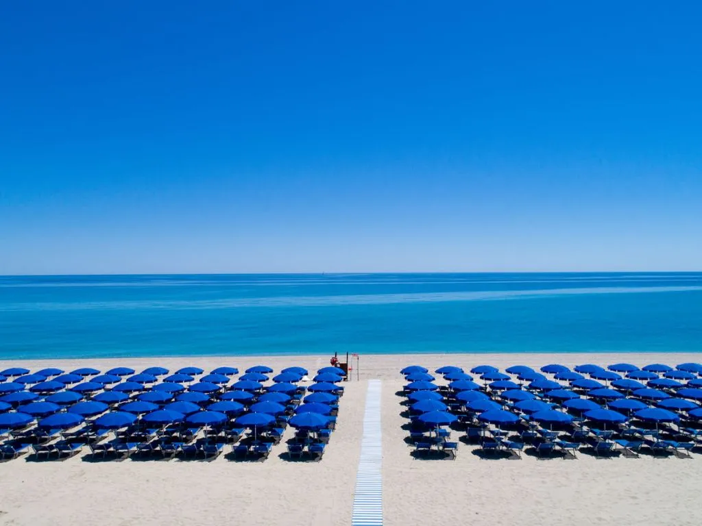 File ordinate di ombrelloni blu sulla spiaggia di sabbia con mare turchese e orizzonte azzurro