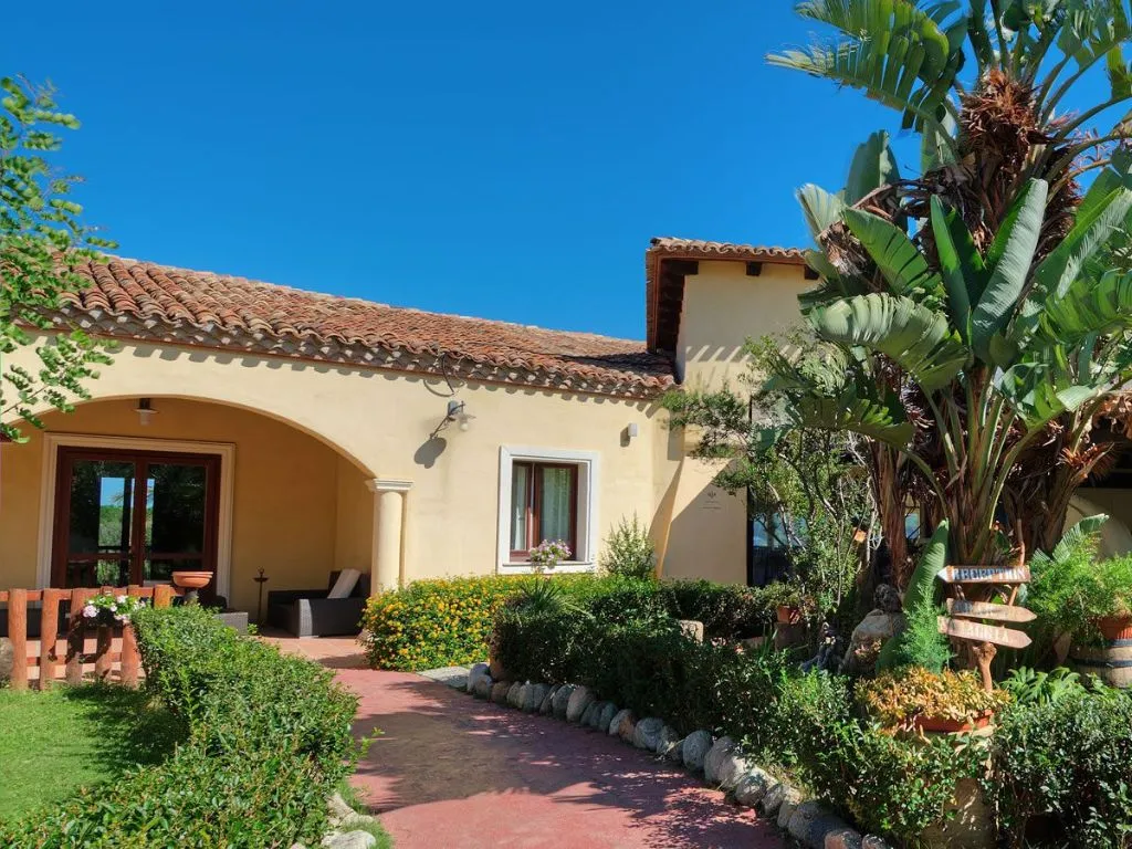 Esterno di una villa con portico ad arco, giardino lussureggiante e piante tropicali