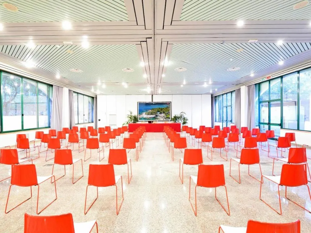 Sala meeting con sedie rosse disposte a platea e schermo per presentazioni