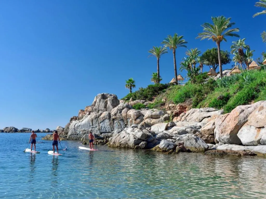 Persone praticano stand up paddle nelle acque limpide vicino alla scogliera con palme