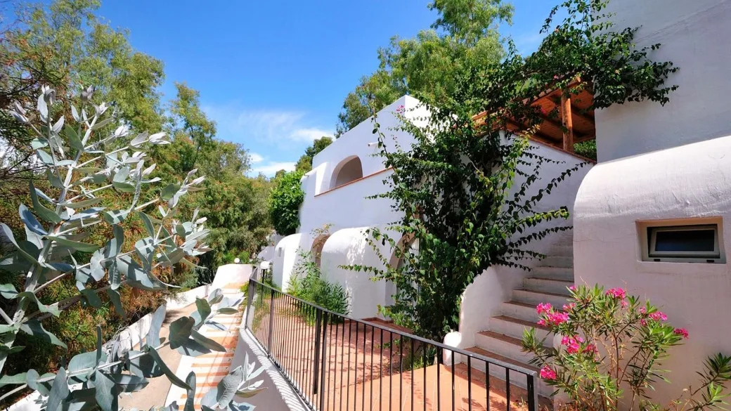 Edificio bianco in stile mediterraneo immerso nella vegetazione con scalinata e fiori