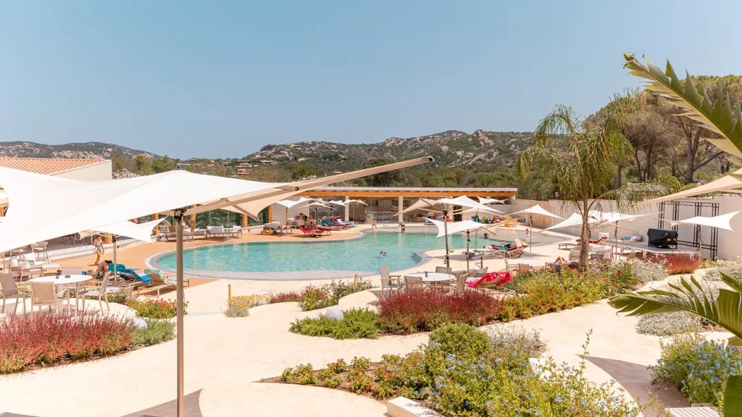 Piscina del resort con ombrelloni bianchi e giardino mediterraneo