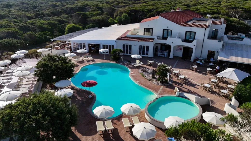 Piscina dalla forma sinuosa con ombrelloni bianchi e terrazza in cotto davanti all'edificio bianco