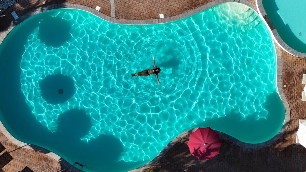 Vista aerea della piscina turchese con persona che nuota e ombrellone rosso