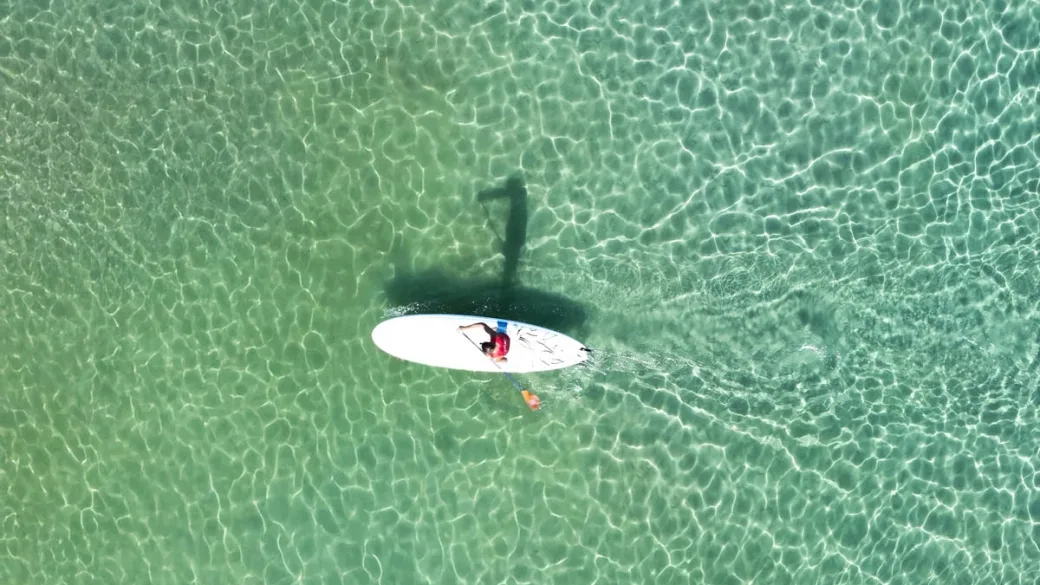 Persona su tavola da SUP nel mare verde cristallino visto dall'alto