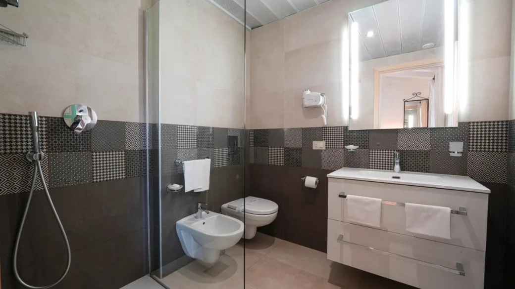 Bagno con doccia a vetro, sanitari sospesi e mobile lavabo bianco con specchio illuminato