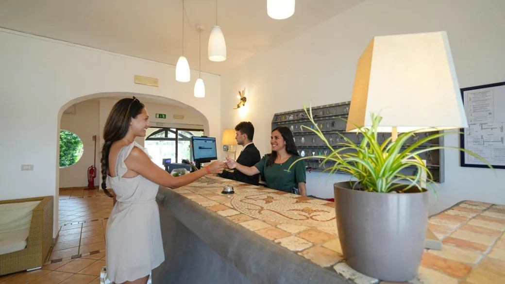 Ospite alla reception accolta dal personale dietro il bancone con mosaico