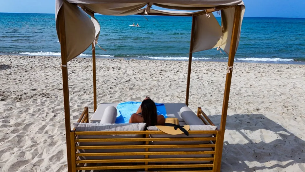 Lettino con baldacchino in legno sulla spiaggia con vista sul mare e surfisti