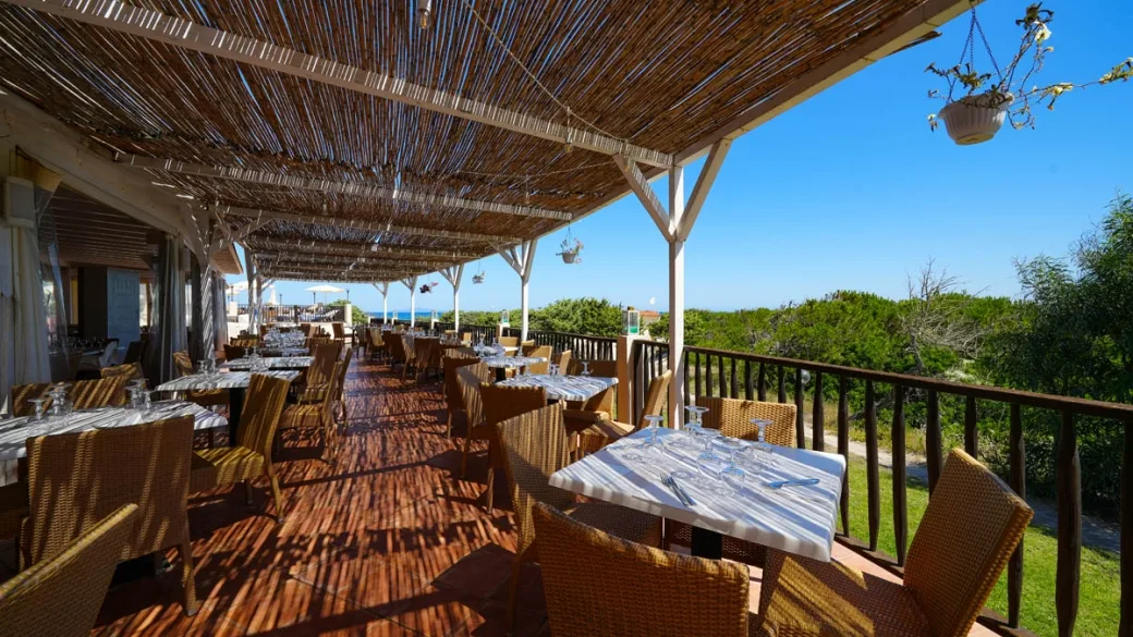 Terrazza ristorante con tavoli apparecchiati sotto pergolato in canne e vista mare
