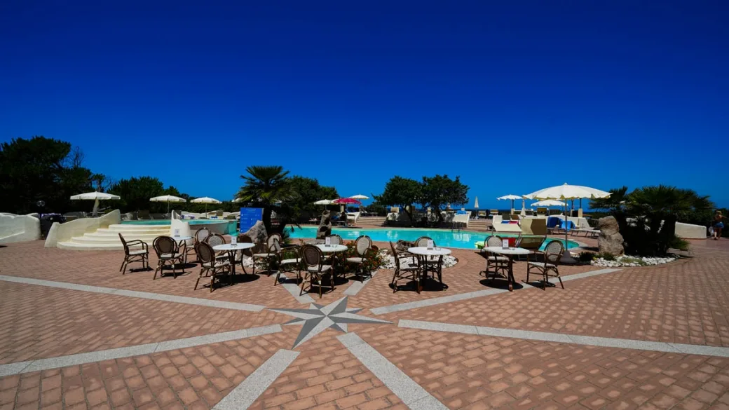 Terrazza con tavolini, ombrelloni e piscina con rosa dei venti pavimentata in cotto