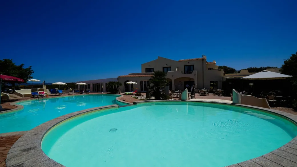 Piscina curvilinea con vasca idromassaggio davanti all'edificio bianco dell'hotel
