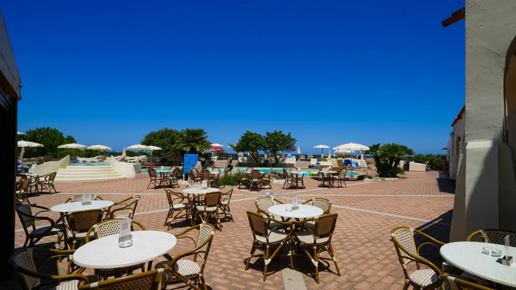 Area bar all'aperto con tavolini e sedie in vimini affacciata sulla piscina
