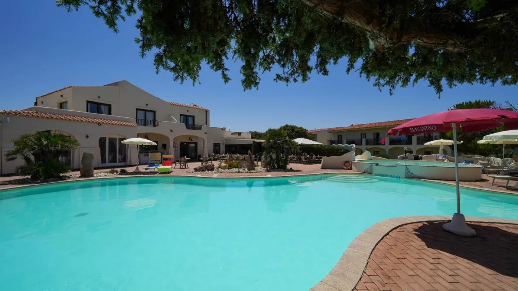 Piscina turchese circondata da terrazza in cotto e edifici dell'hotel con ombrelloni
