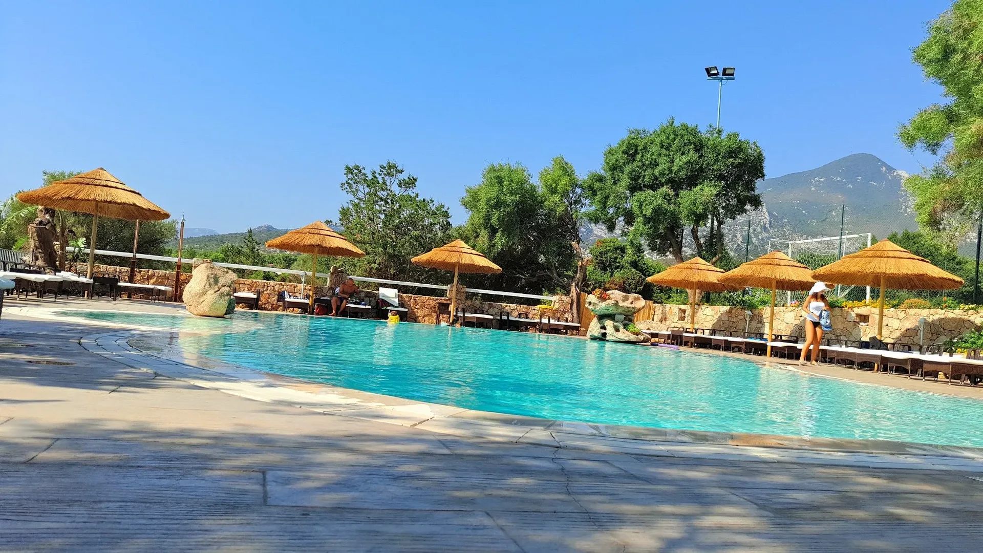 Piscina all'aperto con ombrelloni in paglia e vista sulle montagne circostanti