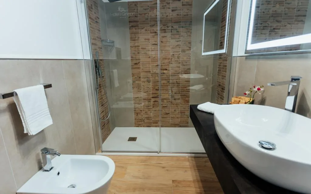 Bagno elegante con doccia walk-in, bidet e lavabo bianco su mensola scura