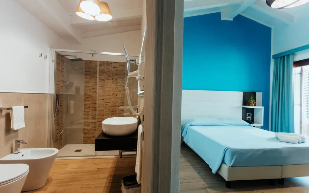Camera con letto matrimoniale, parete azzurra e bagno open space con doccia