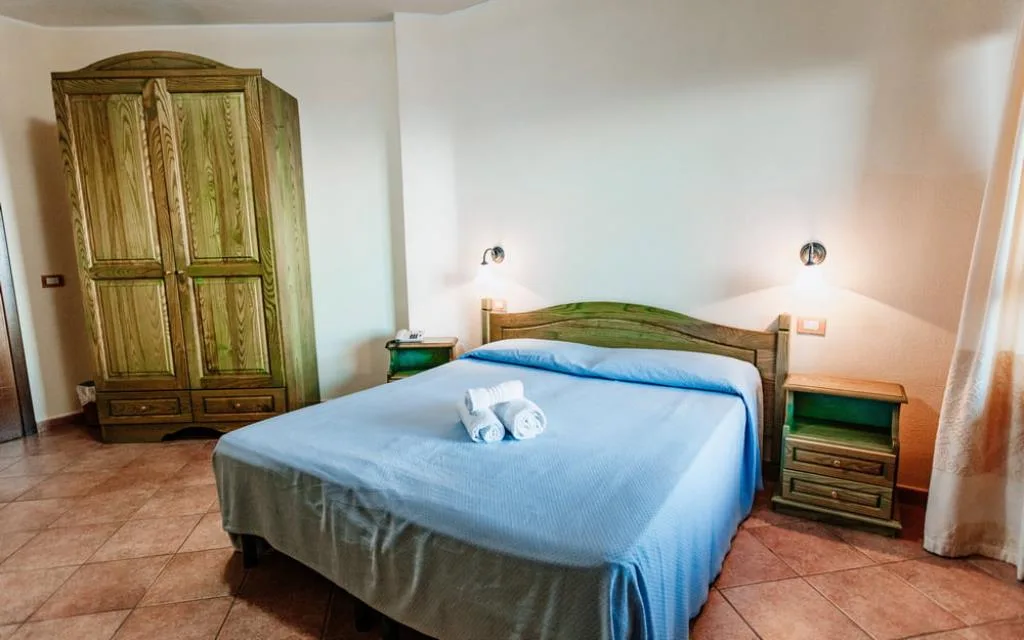 Camera matrimoniale con armadio in legno verde, comodini e letto con copriletto azzurro