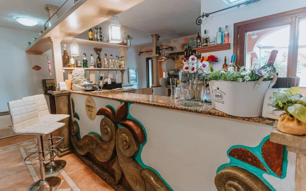Bancone bar decorato con dettagli colorati, sgabelli bianchi e bottiglie sugli scaffali
