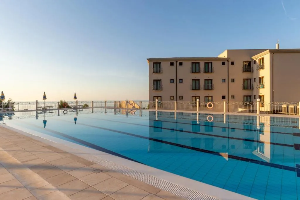 Piscina dell'hotel al tramonto con acqua calma e edificio mediterraneo affacciato sul mare