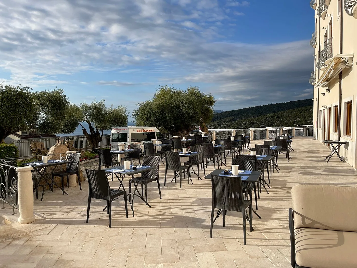 Terrazza ristorante esterna con tavoli e sedie, ulivi e vista mare