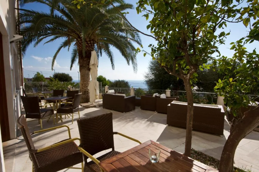Patio esterno con divani in rattan, tavoli, palma e alberi affacciato sul mare