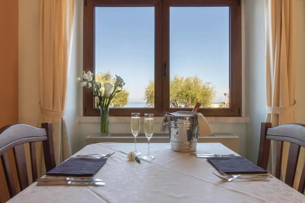 Tavolo del ristorante apparecchiato con spumante e fiori davanti a una finestra con vista mare