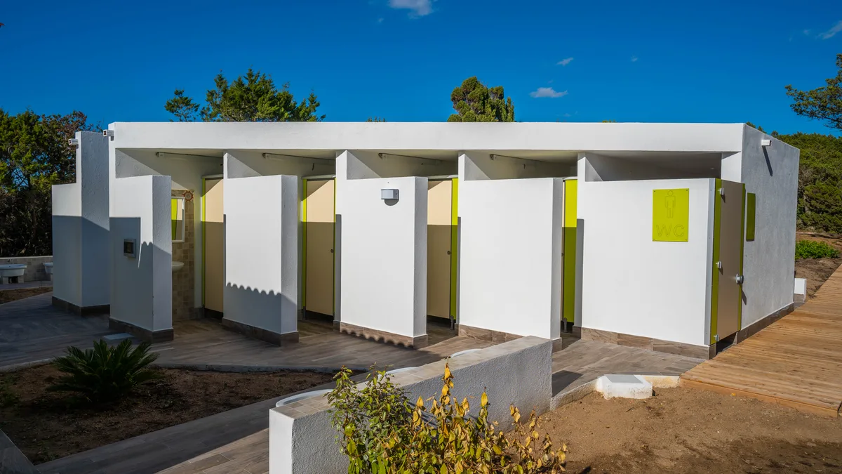 Blocco servizi con docce e wc dalle porte verdi sotto cielo azzurro