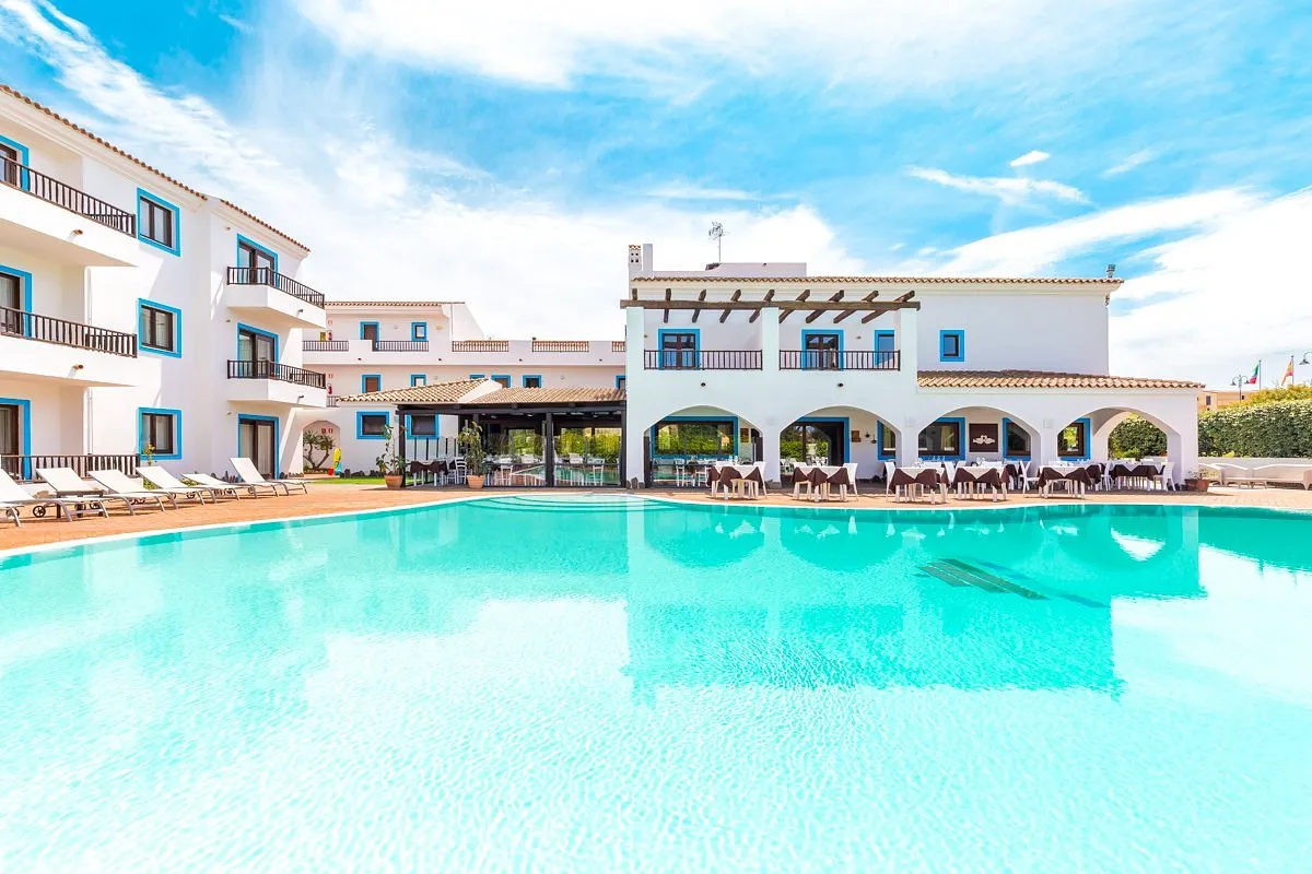 Ampia piscina con acqua turchese e edificio dell'hotel con archi e finestre azzurre
