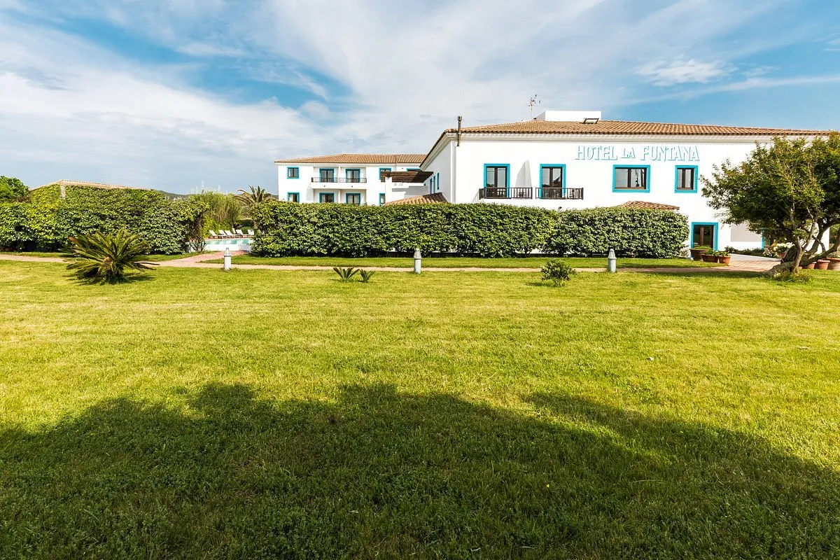 Facciata dell'Hotel La Funtana con prato verde, siepi e cielo azzurro