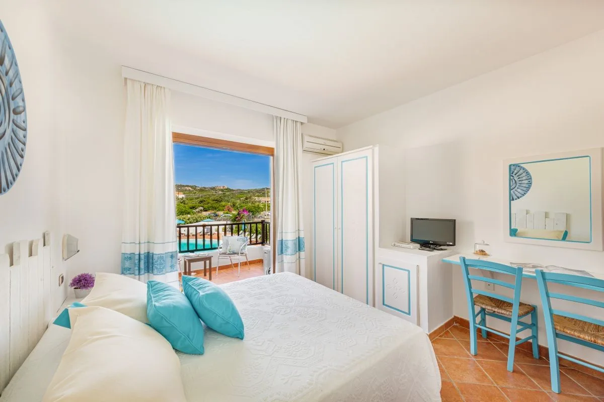 Camera doppia in stile mediterraneo con balcone vista piscina e arredi bianchi e azzurri
