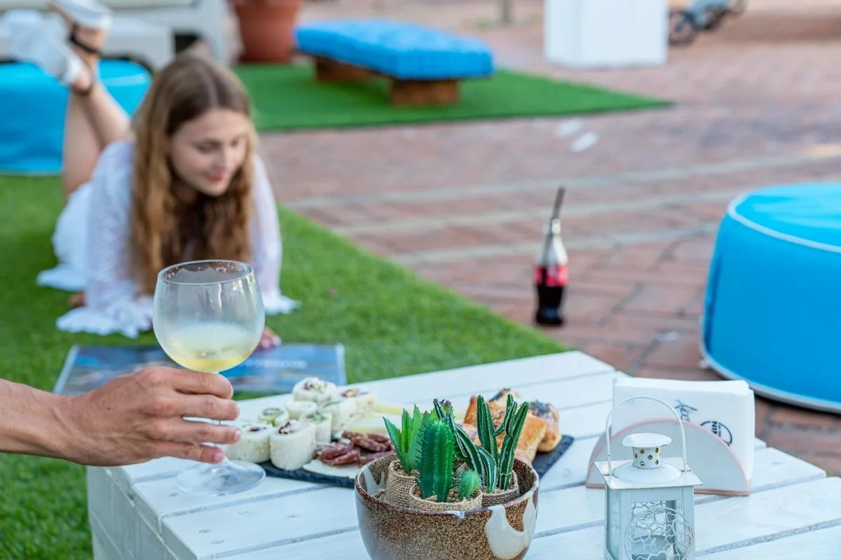 Aperitivo all'aperto con calice di vino e tagliere su tavolino bianco, ospite sul prato sullo sfondo