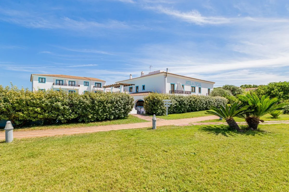 Vista esterna dell'Hotel La Funtana con giardino verde, palme e viale d'accesso