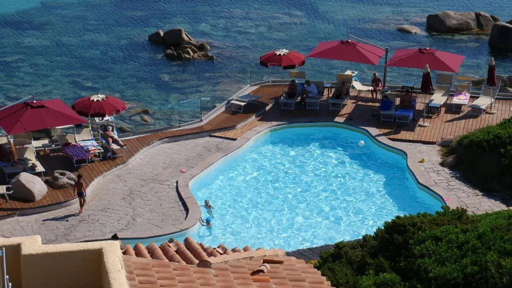 Veduta dall'alto della piscina con ombrelloni rossi affacciata sul mare roccioso