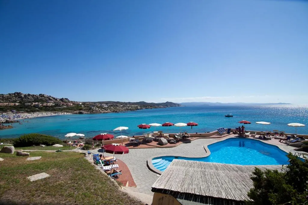 Piscina del resort con ombrelloni e vista panoramica sulla spiaggia e mare cristallino
