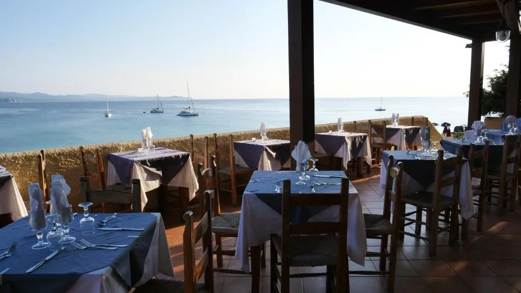 Terrazza del ristorante con tavoli apparecchiati e vista sul mare con barche