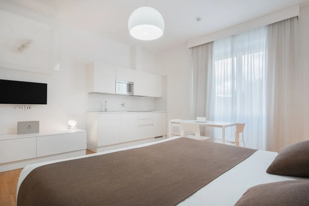 Monolocale bianco con letto, angolo cottura e tavolo vicino alla finestra